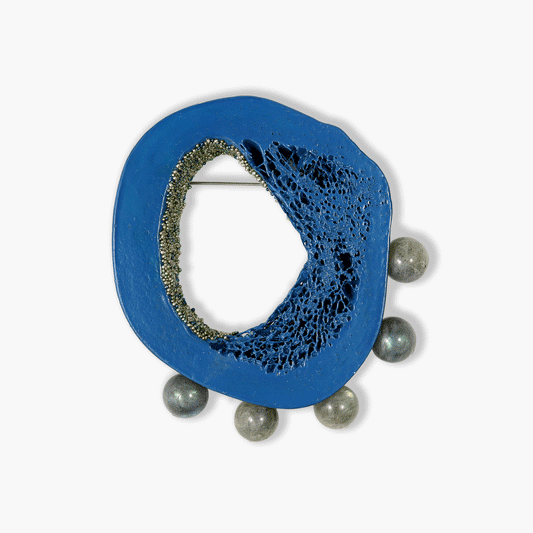 Close-up image of a unique brooch by Chantel Gushue, featuring a painted matte blue slice of lacy cow bone adorned with glittering glass beads inside its hollow. Five round beads of grey labradorescent labradorite accent the piece. Sterling silver brooch mechanism with a stainless steel pin stem. Handcrafted by the artist in Nova Scotia. Dimensions: 2-3/4 x 3 inches.