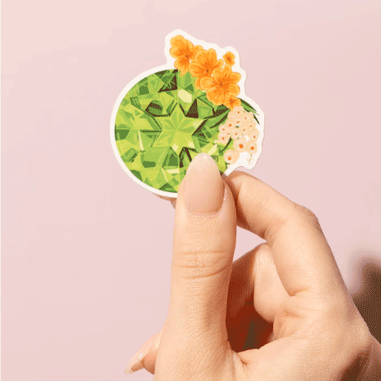 Thumb and forefinger holding a Sticker showcasing an illustrated August birthstone of peridot and birth flowers of gladiolus and poppy.