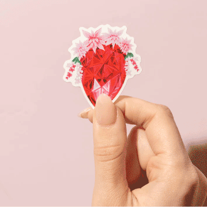 Thumb and forefinger holding a Sticker showcasing an illustrated July birthstone of ruby and birth flowers of water lily and larkspur