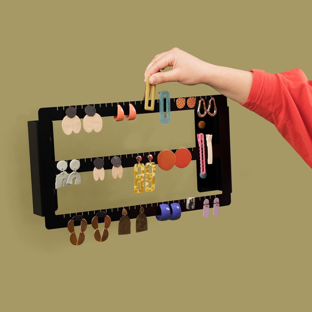 Image of an arm adding a hairclip to a wall-mounted jewellery organizer.