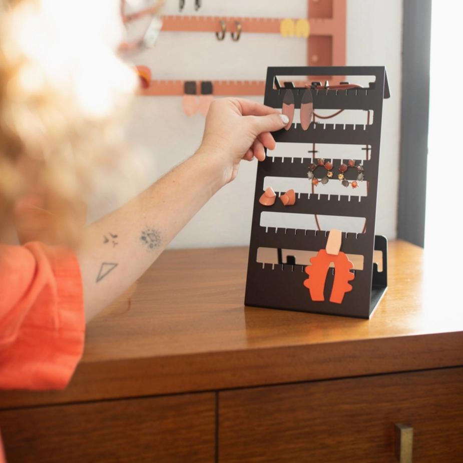 A woman adds  pair of earrings to a black Safran Everyday table top jewellery organizer