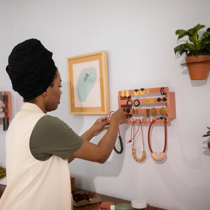 A woman adding a necklace to a wall-mounted earring and necklace storage unit by Sanfran Everyday