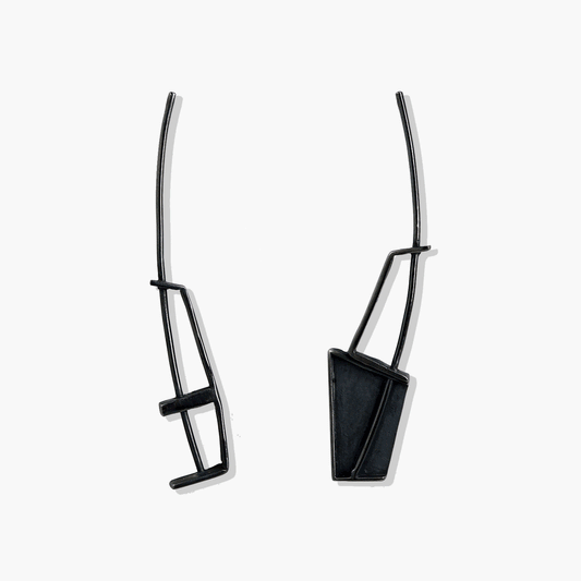 Close up view of asymmetrical long blackened sterling silver earrings by Therese Cruz: Contemporary design with one earring longer than the other. Bold and dramatic blackened finish contrasts with shiny sterling silver. Versatile for any occasion, handcrafted in Nova Scotia.
