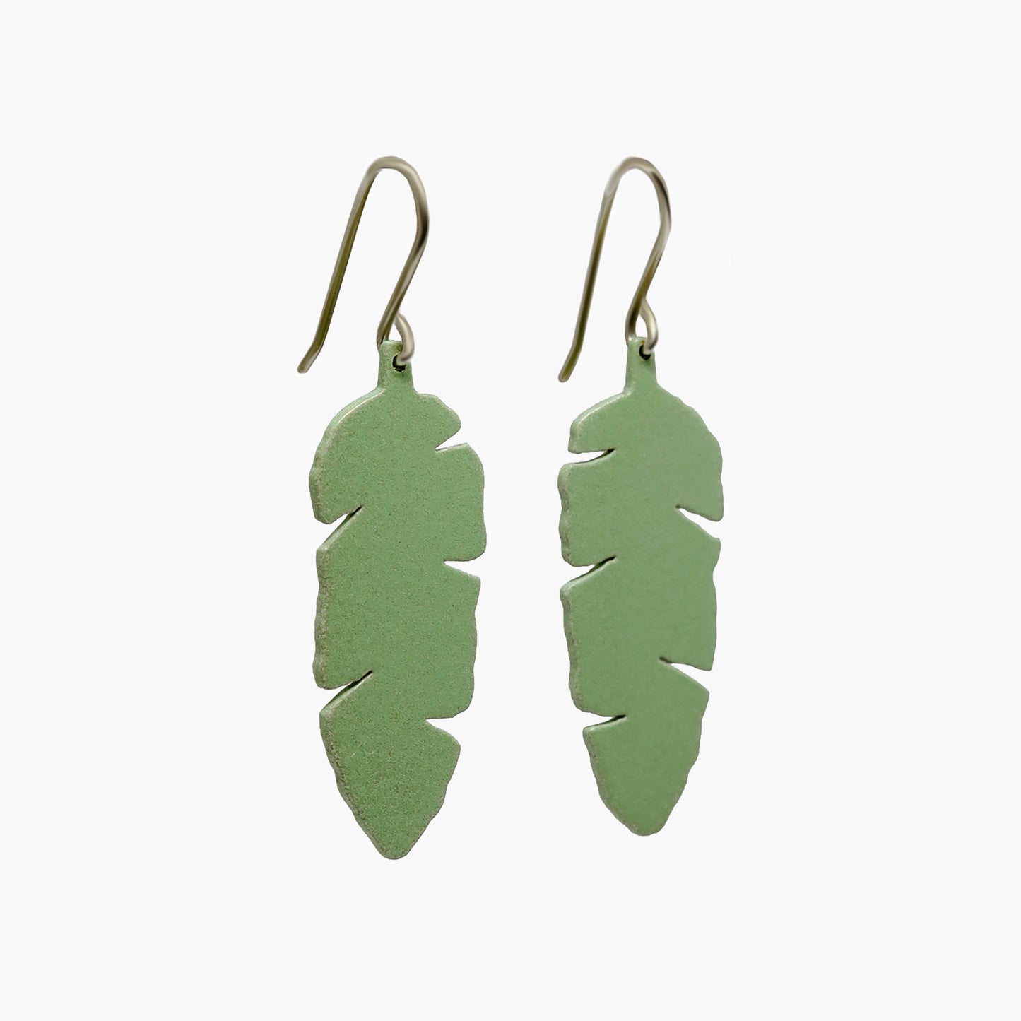 Pair of pale green drop earrings with a unique banana leaf silhouette. The earrings are made of a glossy, lightweight material and hang delicately from silver hooks. The leaf-like shape features curved edges and a pointed tip, creating a natural and organic aesthetic. These earrings are perfect for adding a touch of tropical flair to any outfit.