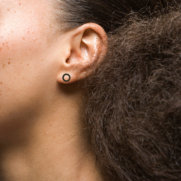 A close up view of Dorothée Rosen's Hello stud earrings on a female's earlobe. The photo shows the small scale of the earrings.