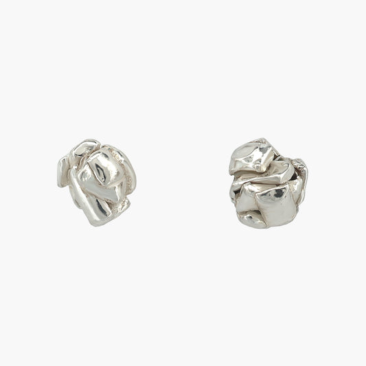 A pair of Dorothée Rosen's rock earrings. The earrings are small sterling silver studs of overlapping folds of metal. The earrings are shown on a bright background.