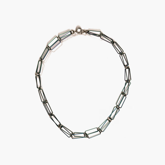 An image of a silver-colored necklace made of fine steel wire. The necklace is a delicate chain composed of open links of steel wire. It has a smooth, shiny surface and catches the light in various angles. The necklace features a simple and elegant oversized clasp. The clasp is an oversize spring ring with a smooth and reflective surface that complements the necklace's overall aesthetic.