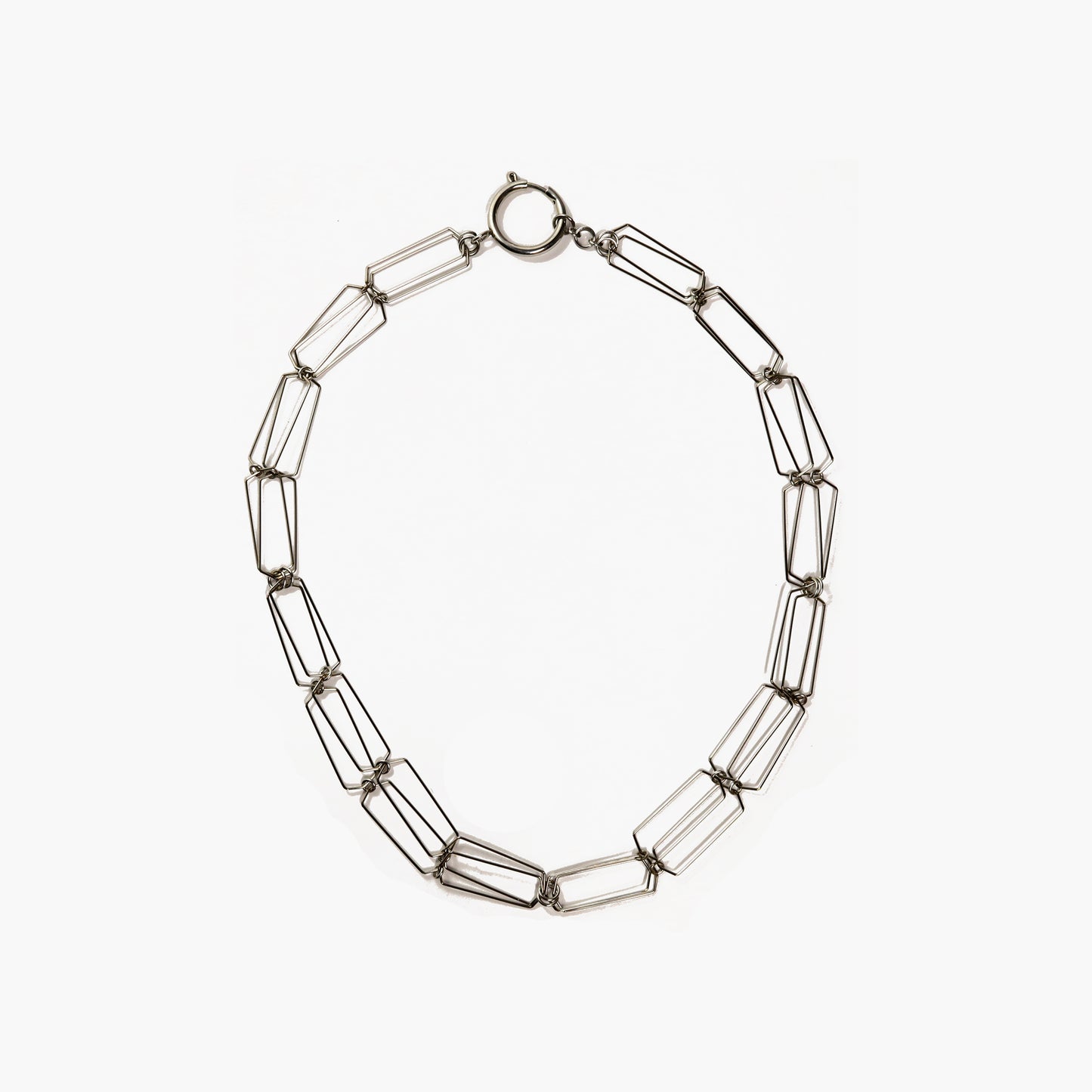 An image of a silver-colored necklace made of fine steel wire. The necklace is a delicate chain composed of open links of steel wire. It has a smooth, shiny surface and catches the light in various angles. The necklace features a simple and elegant oversized clasp. The clasp is an oversize spring ring with a smooth and reflective surface that complements the necklace's overall aesthetic.