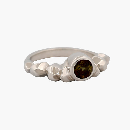 Sterling silver ring with a carved band and a 5mm Andalusite gemstone nestled among the edges.