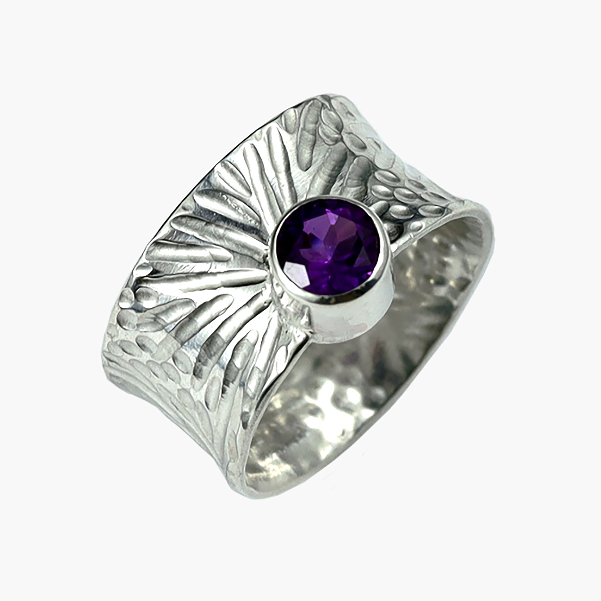 Close-up of the 'Spring' sterling silver ring by Erin Christensen, showcasing a wide band with a textured burst design, highlighted by a vibrant gemstone. The convex shape and intricate hand-chased detailing add to its unique aesthetic. Available in two sizes with gemstone options including bright purple amethyst.