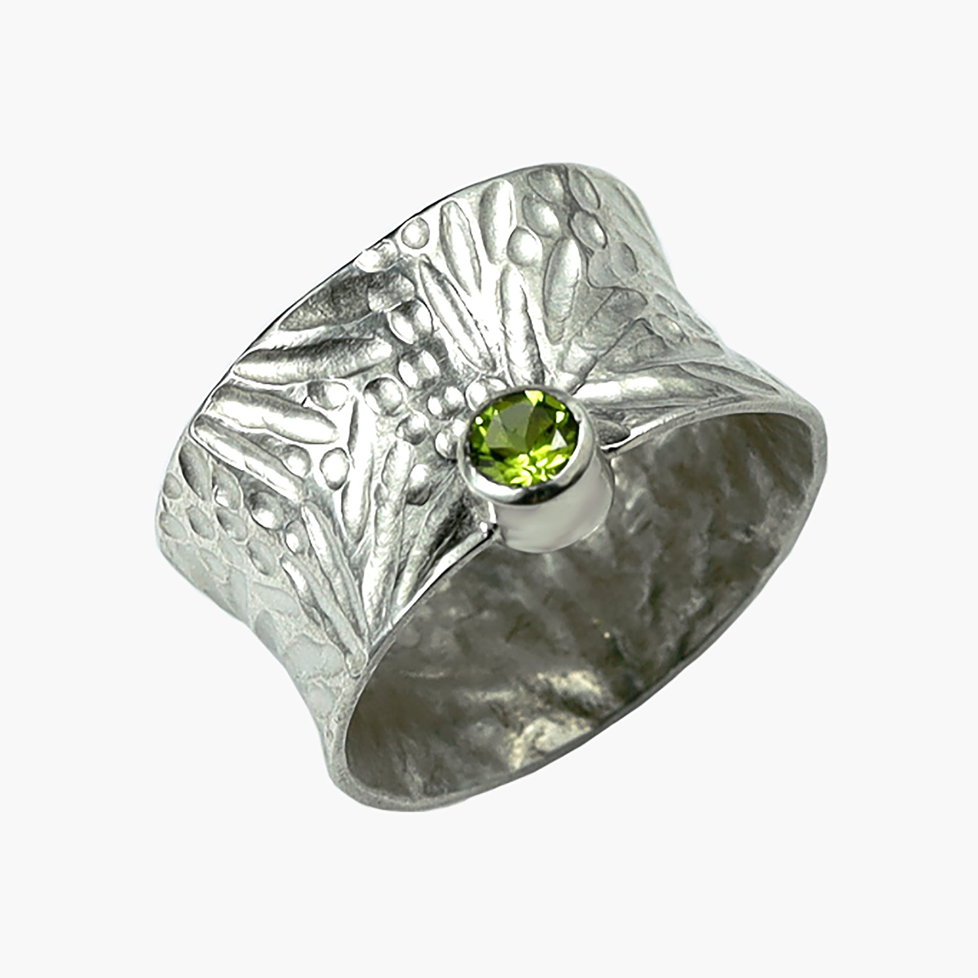 Close-up of the 'Spring' sterling silver ring by Erin Christensen, showcasing a wide band with a textured burst design, highlighted by a vibrant gemstone. The convex shape and intricate hand-chased detailing add to its unique aesthetic. Available in two sizes with gemstone options including bright green peridot.