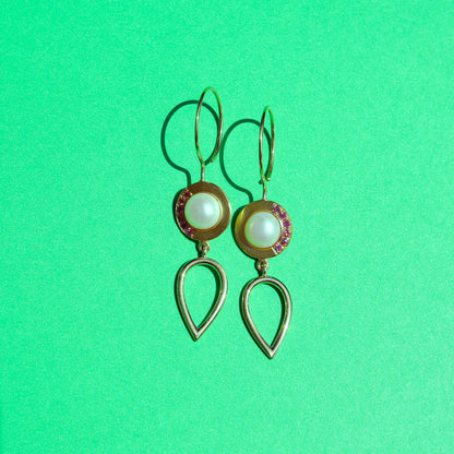 One pair of gold and pearl earrings brightly lit with a long shadow.