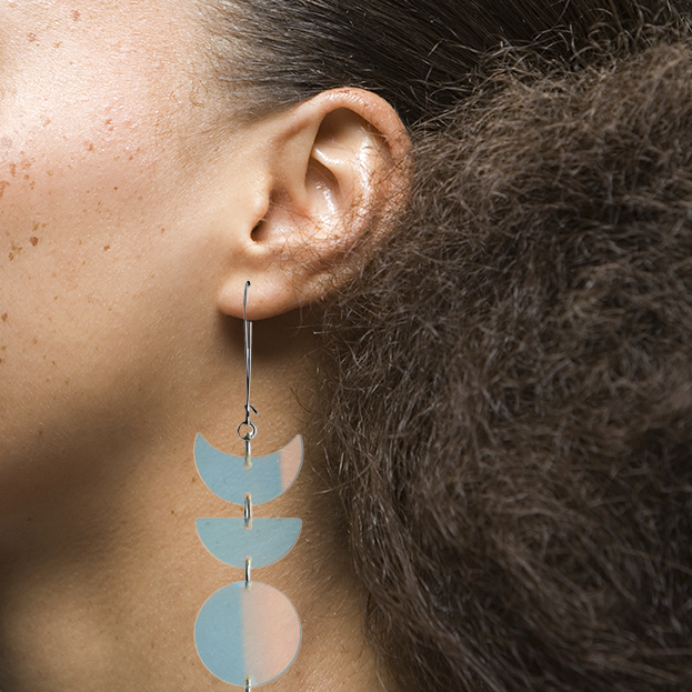 Model view image of Indi City Moonphase Earrings in iridescent transparent acrylic. These long drop earrings beautifully capture a fusion of cultural and contemporary styles, symbolizing the ever-changing phases of the moon.